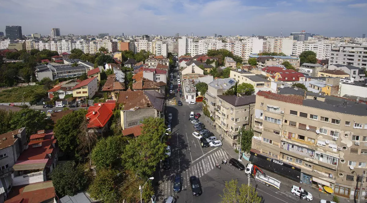 O intersecție din București, mai multe mașini, o trecere de pietoni, blocuri, un spațiu verde