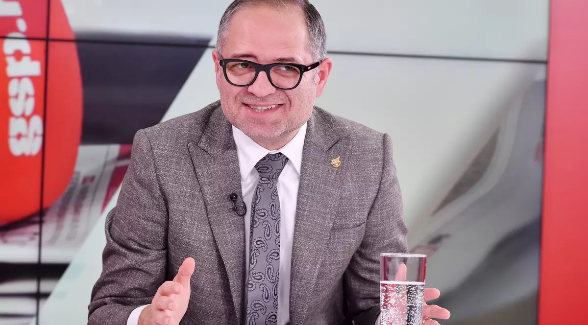 Bogdan Matei, un bărbat îmbrăcat într-un sacou gri, cu cămașă albă, cravată gri cu niște forme desenate cu negru, poartă ochelari de vedere cu rame pătrate și negre. Vorbește și gesticulează din mâini. În fața lui, pe o masă se află un pahar cu apă. În spatele său este un panou gri cu o siglă roșie pe care scrie GSP.ro