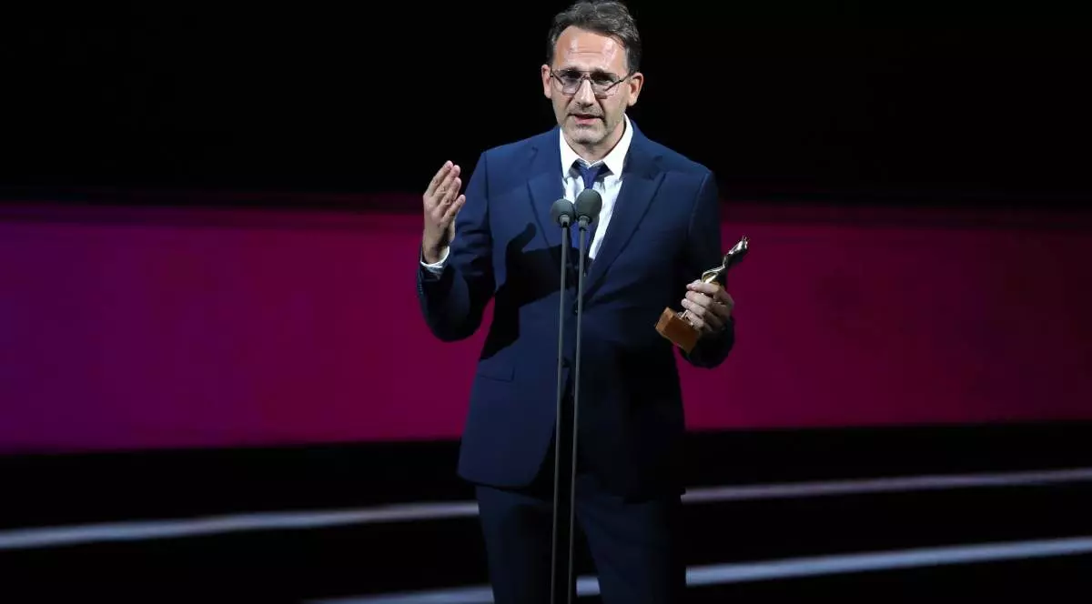 Bogdan Mureșanu surprins în timpul galei Premiilor Gopo vorbind la microfon și ținând în mâna dreaptă trofeul