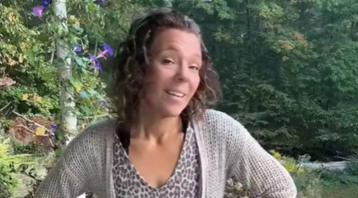 Poză cu Brittany Bland, femeia care nu a mai folosit deodorant. Are părul desprins, poartă o rochie și o bluză gri. În spate, se află mai mulți copaci