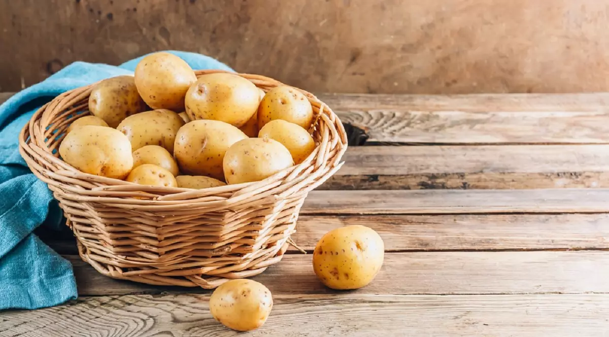 Care este diferenţa dintre cartofii noi şi cei obişnuiţi - Imagine cu un coşuleţ de nuiele plin cu cartofi noi şi aşezat pe o masă de lemn