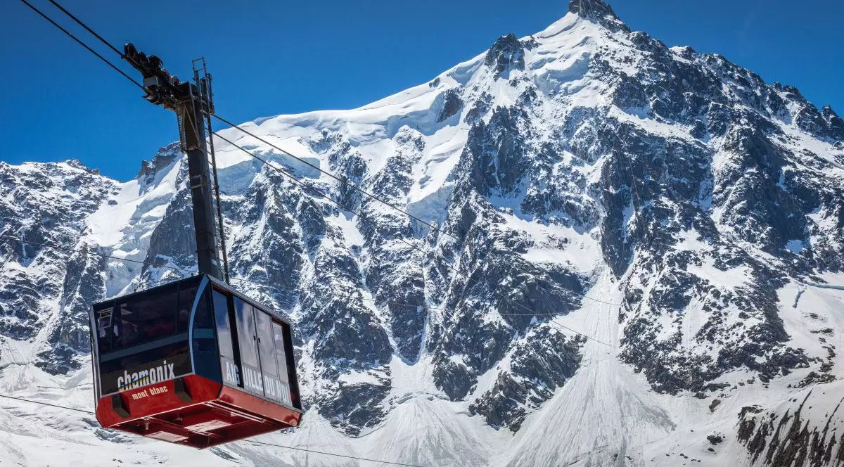 O telecabină negru cu roșu este pe fir către Aiguille du Midi, Masivul Mont Blanc, Chamonix, estul Franței, iar în depărtare se văd munții acoperiți cu zăpadă