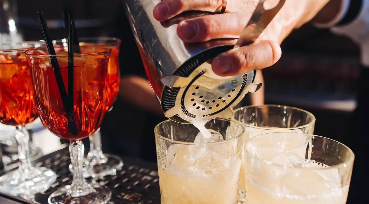 Barman la lucru, un șir frumos de cocktailuri cu băuturi alcoolice de diferite culori la o petrecere în aer liber într-un bar, precum și alții la un serviciu de catering pentru un banchet în cadrul unui eveniment; barman preparând băuturi într-un club