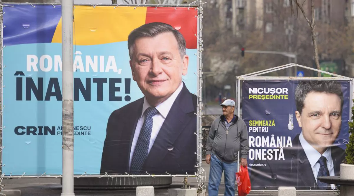 Bărbat surprins între două panouri electorale pe care apar Crin Antonescu și Nicușor Dan, candidați la alegerile prezidențiale din 4 mai 2025