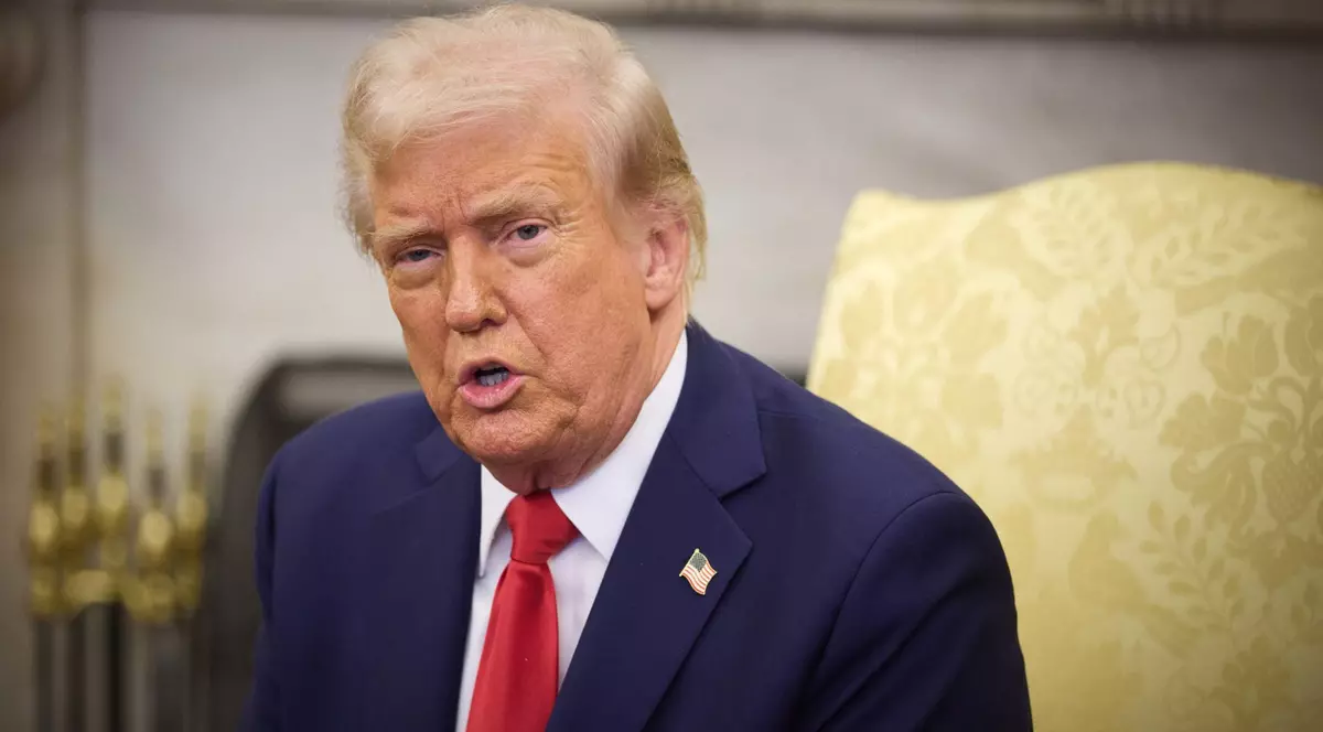 Președintele SUA Donald Trump stând pe scaun, purtând un sacou albastru, cu o cravată roșie și o cămașă albă