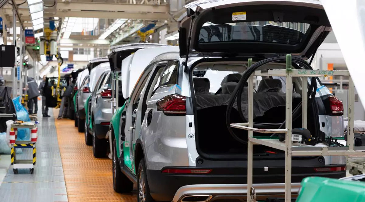 Fabrică auto, unde mai multe SUV-uri argintii aflate una în spatele celeilalte, sunt în diverse faze de asamblare.