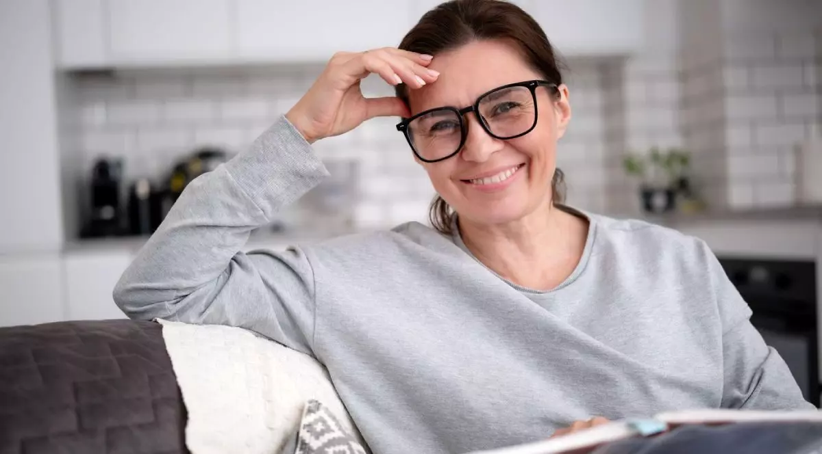femeie fericită cu ochelari citind o carte și zâmbește acasă