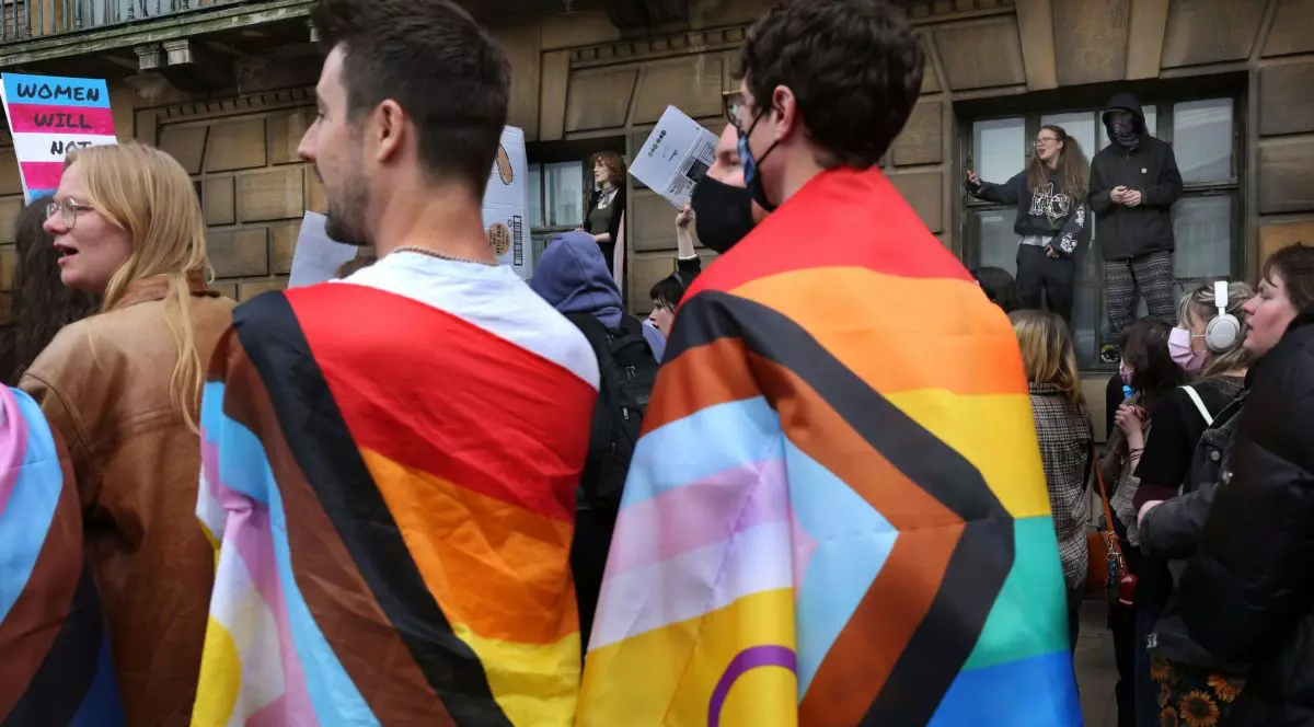 Protestatarii înfășurați în steaguri trans ascultă discursurile ținute în fața Crții Supreme, în timp ce alții se urcă pe pervazele clădirii în timpul protestului