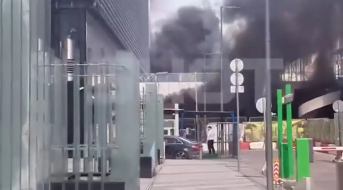 În imagine este ilustrată o parcare în care se observă fum negru, în urma unui incendiu