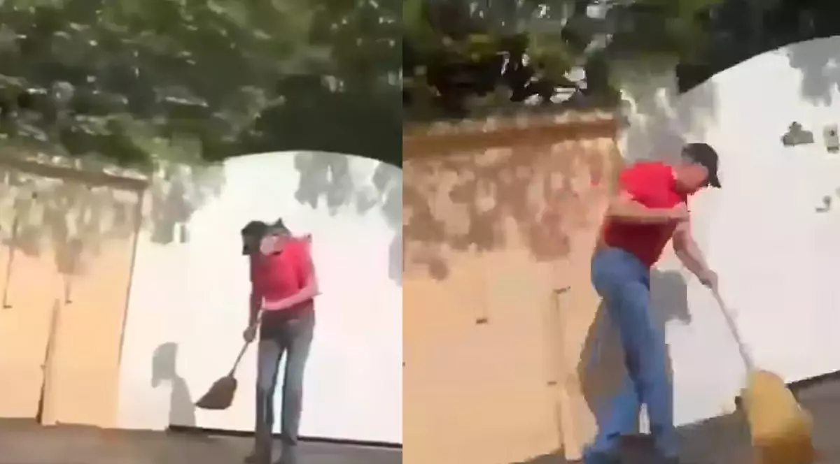 Klaus Iohannis, îmbrăcat în blugi și tricou roșu, cu o șapcă neagră în cap, cu o mătură în mână, în fața unei porți albe