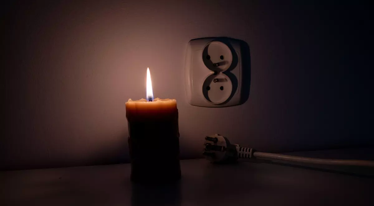 Poză cu o lumânare aprinsă în timpul unei pene de curent. Lângă lumânare e o priză