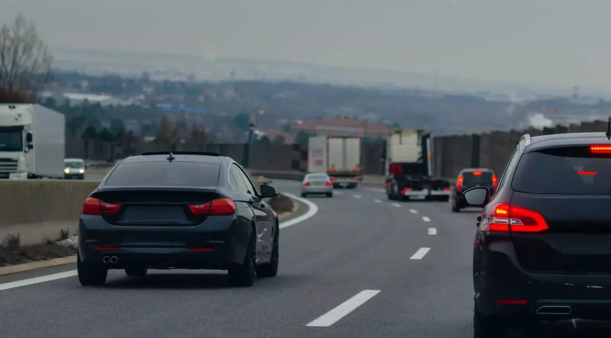 Autotradă aglomerată cu două benzi pe sens desparțite de un parapet.În prim plan sunt doua mașini negre, una care circulă pe banda doi, iar cealaltă pe banda unu.