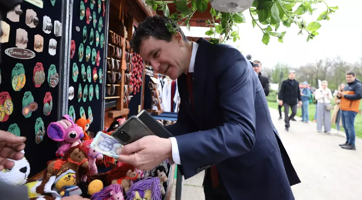Nicușor Dan, îmbrăcat într-un costum negru, cu bani în mână, vrea să cumpere ceva de la o tarabă