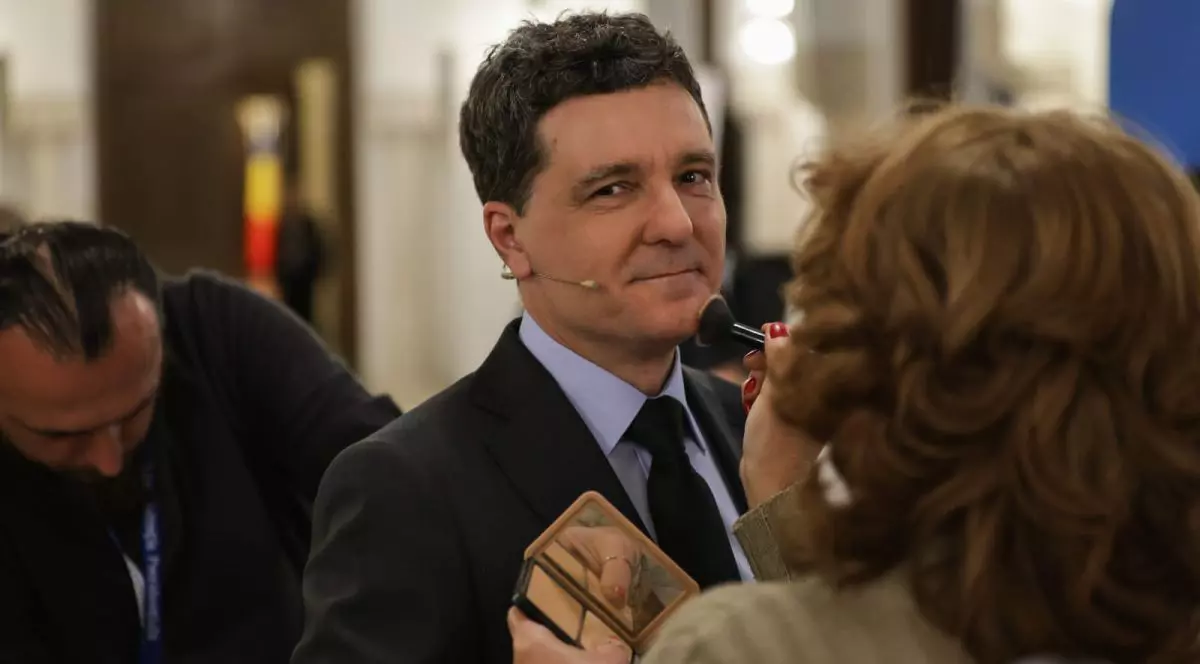 Nicușor Dan așteaptă să fie machiat pentru dezbatere. O femeie îi trece o pensulă de întins fondul de ten pe față