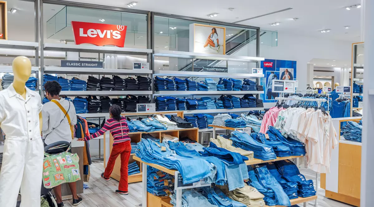 Oameni la cumpărături pentru Levi's denim la magazinul Macy's în secțiunea de vânzare cu amănuntul spațioasă și luminoasă cu blugi stivuiți. New York. SUA.
