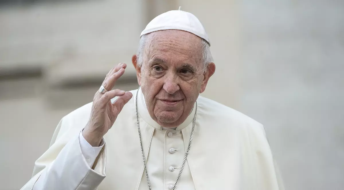 În imagine este ilustrat Papa Francisc, în timp ce ține mâna dreaptă ridicată