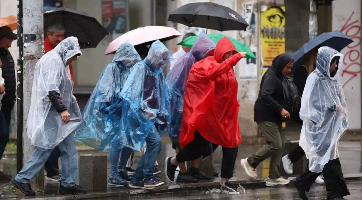 Oameni surprinși în timp ce țin în mâini umbrele și sunt îmbrăcați cu pelerine de ploaie, în zona Piața Romană din București, martie 2025