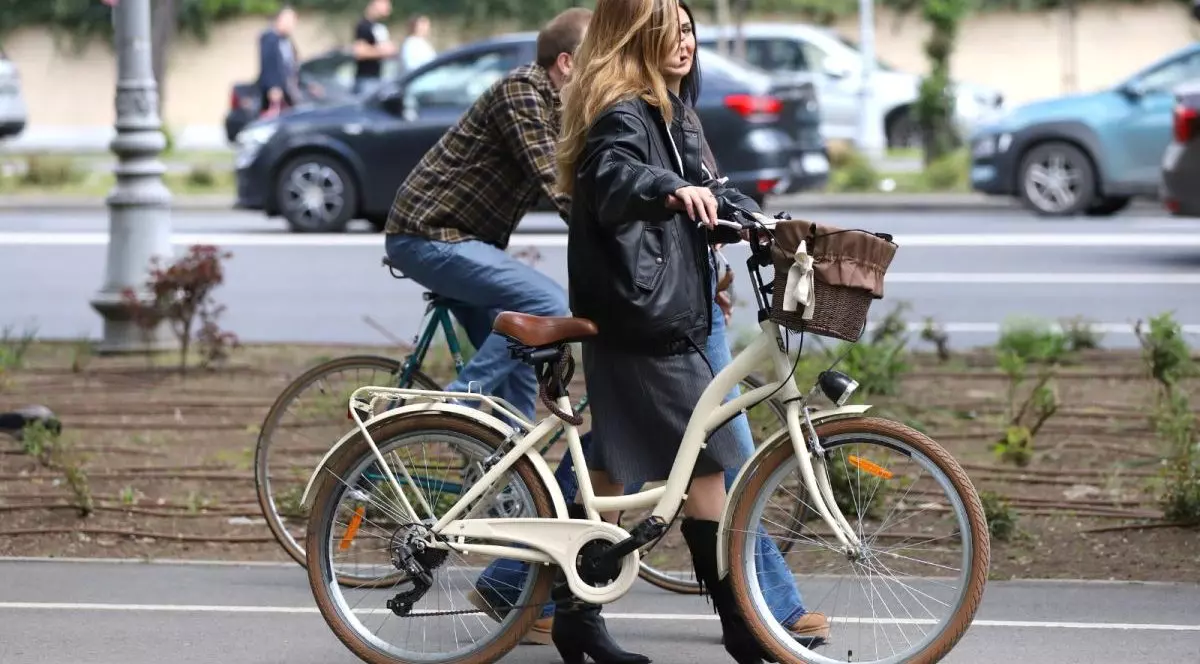 O tânără merge pe lângă bicicleta pe care o ține de coarne și vorbește cu o prietenă, iar paralel cu ele, pe aceeași stradă, un tânăr merge pe biciletă. În spate, se văd mașini care circulă pe stradă și alți oameni, într-o zi însorită de primăvară