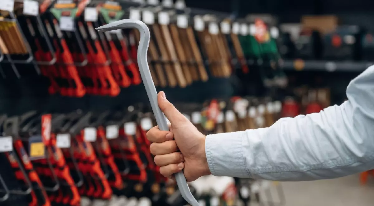 Un bărbat ține o rangă în mână, poartă o câmașă albă. Vedere detaliată de aproape a mâinii omului în magazinul de unelte