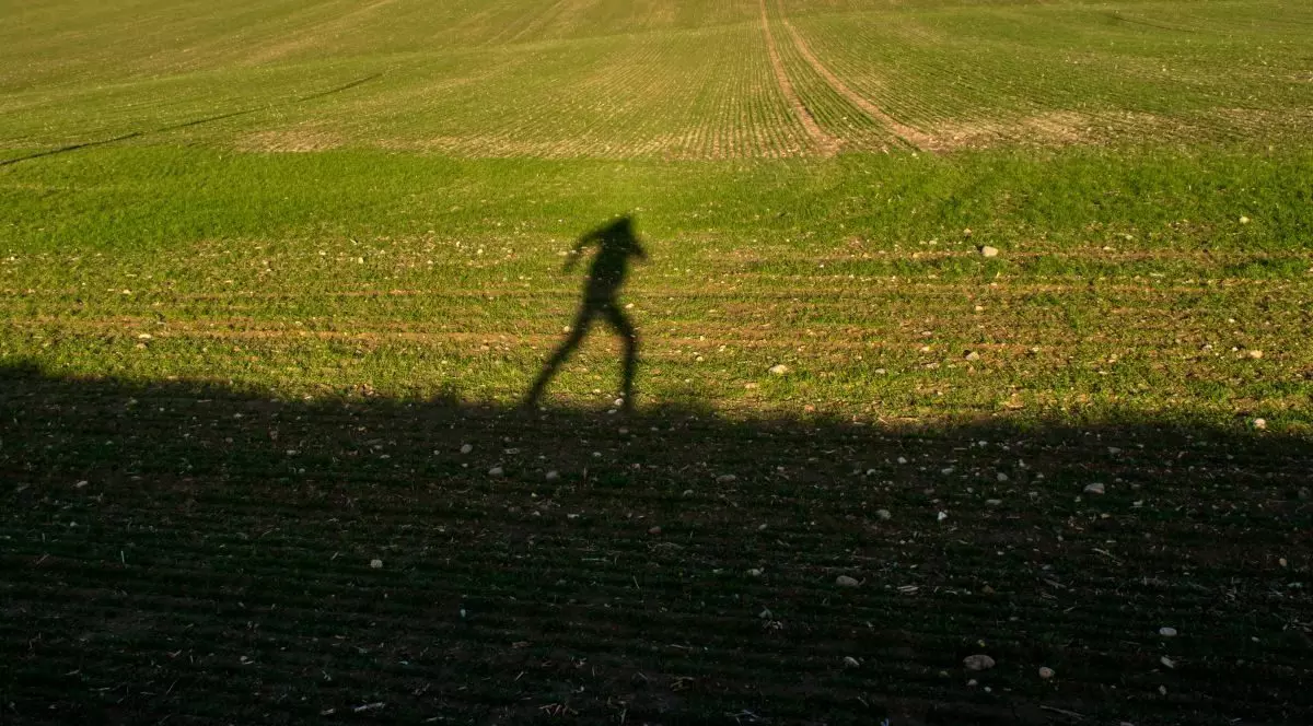 Umbra unei persoane care aleargă pe un câmp verde sub lumina slabă a soarelui