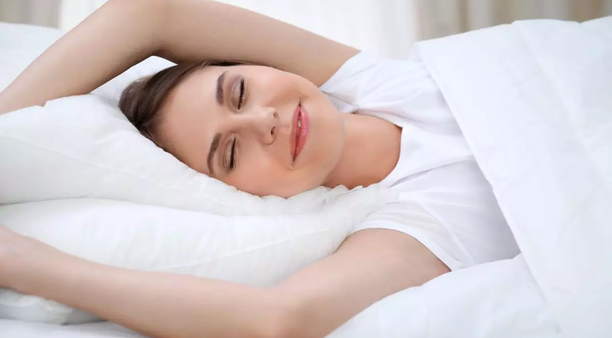 Femeie care se întinde în pat după trezire, intrând într-o zi fericită și relaxată după un somn bun.