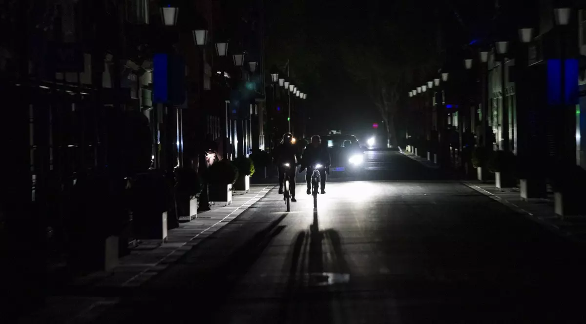 Stradă în beznă din cauza penei de curent în orașul Albacete, pe 28 aprilie 2025. Doi bicicliști merg în fața unei mașini care luminează drumul cu ajutorul farurilor