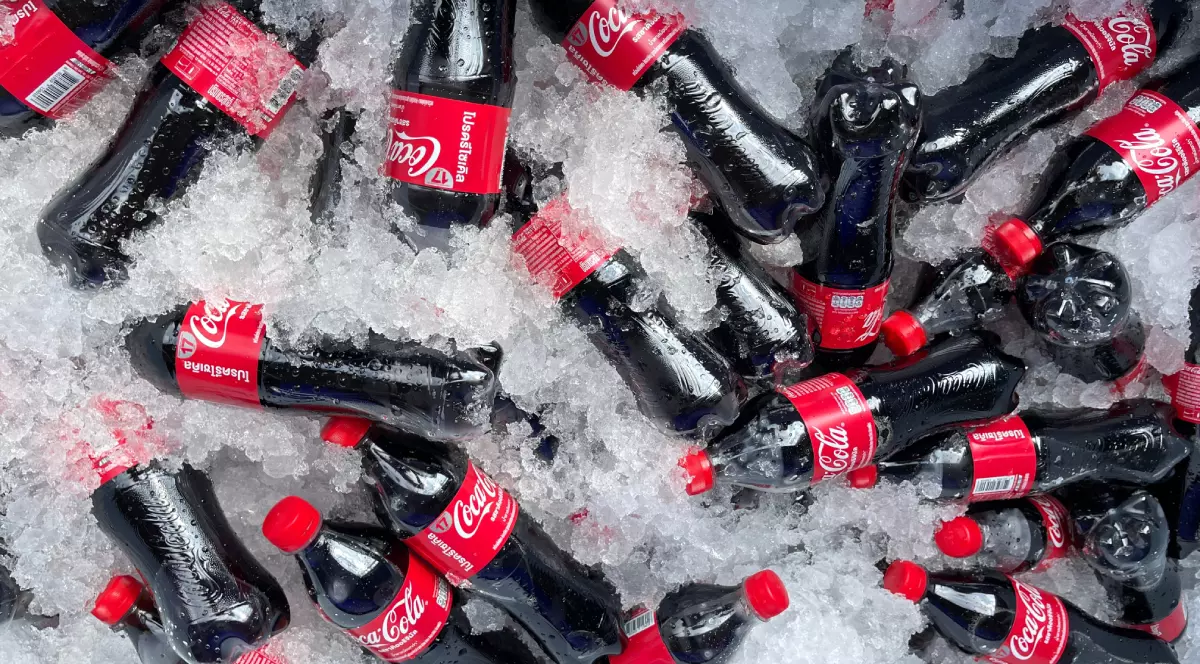 Mai multe sticle de suc Coca-Cola așezate printre cuburi de gheață