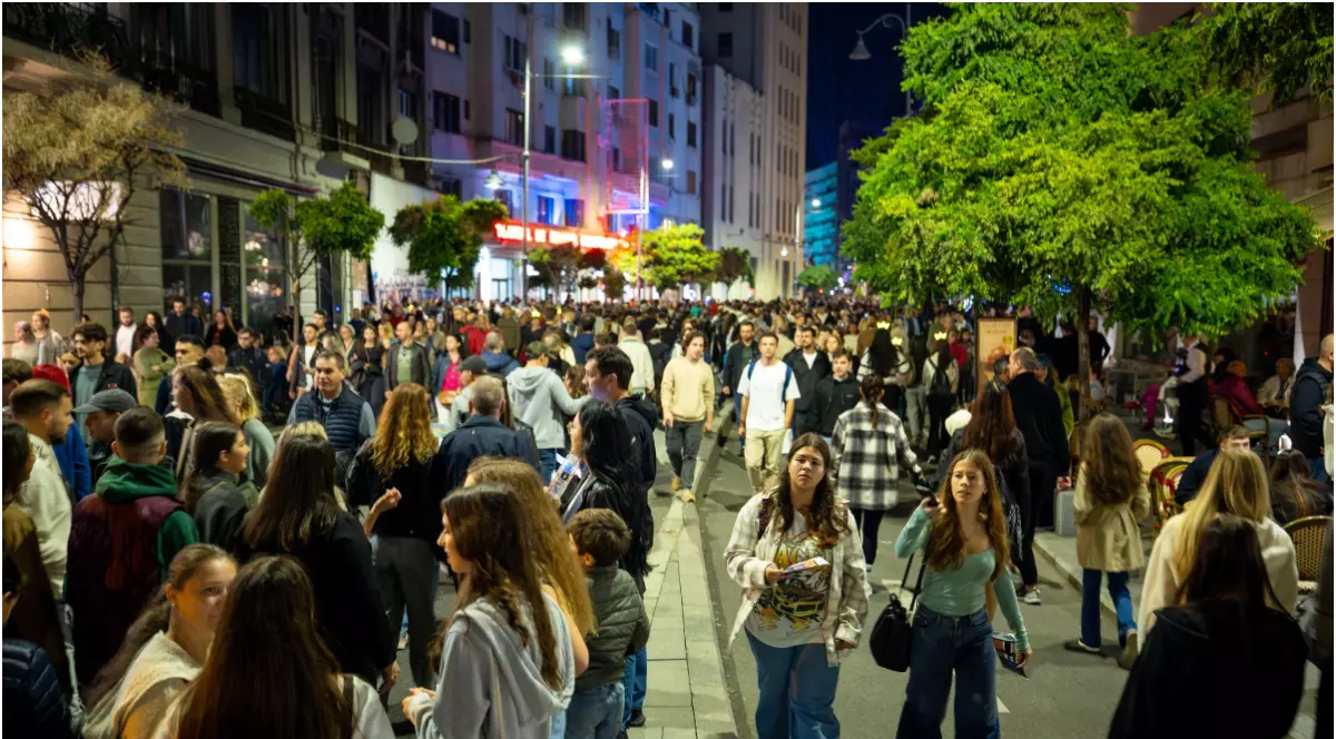 În imagine sunt ilustrați mai mulți oameni care se plimbă pe o stradă pietonală