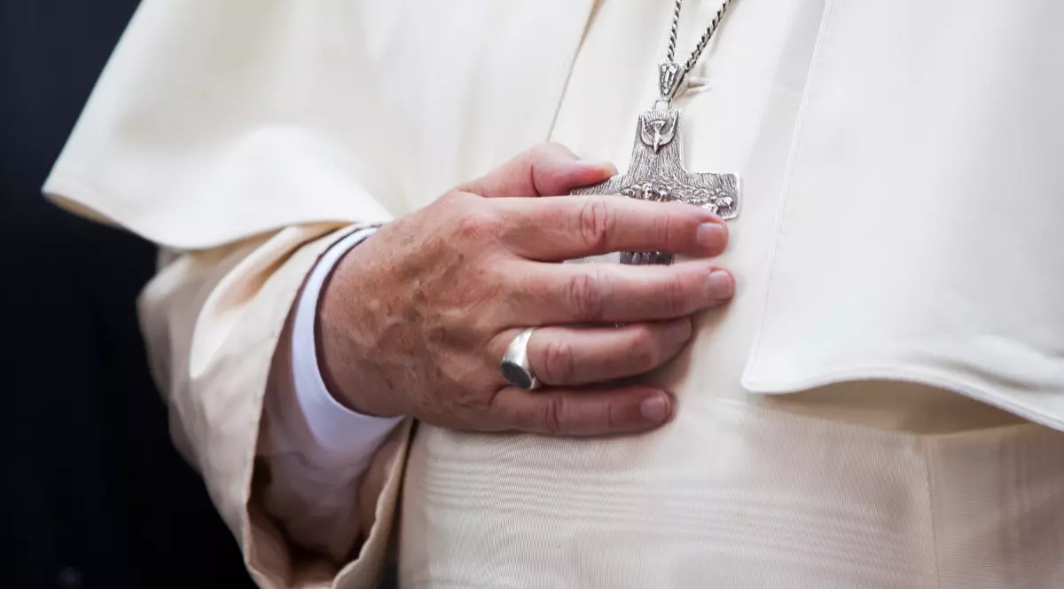 În imagine este ilustrată ținuta albă, cu o mână care atinge crucea de la gât
