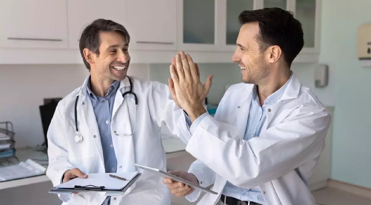 Doi colegi de vârstă mijlocie, lucrători medicali prietenoși, au bătut palma, s-au întâlnit în sala de consultații modernă cu tabletă și clipboard. Lucru în echipă eficient, pozitiv, recunoaștere reciprocă pentru lucrul bine făcut împreună