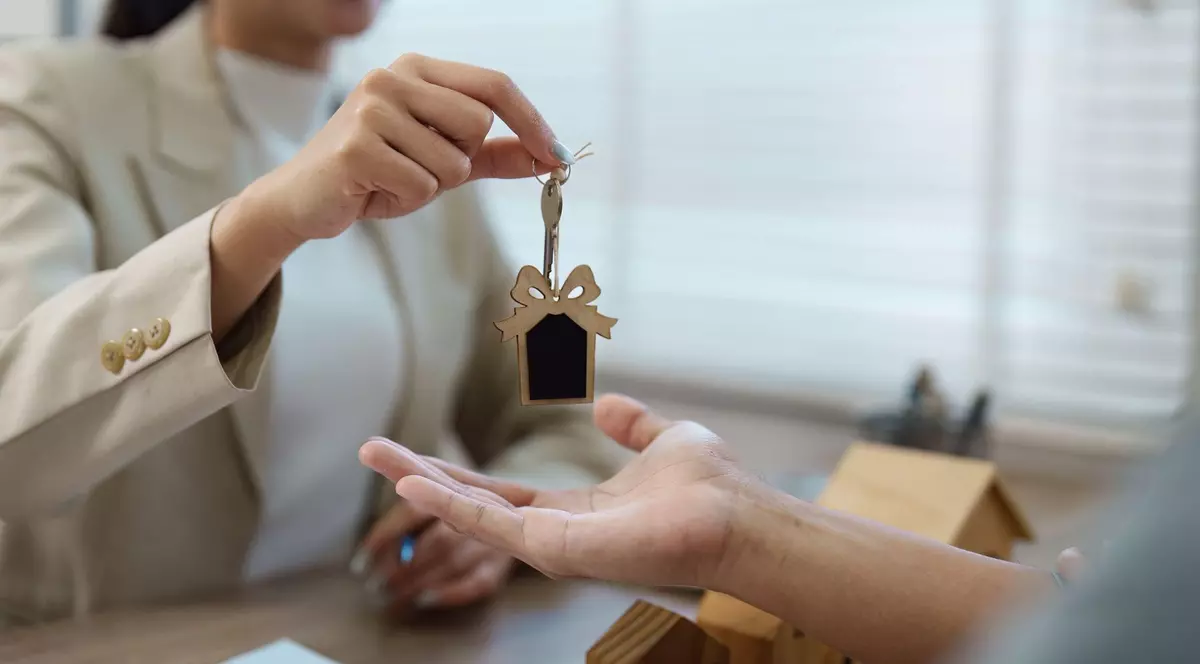 Un agent imobiliar ține cheile unei case deasupra unei mâini întinse a unui client.
