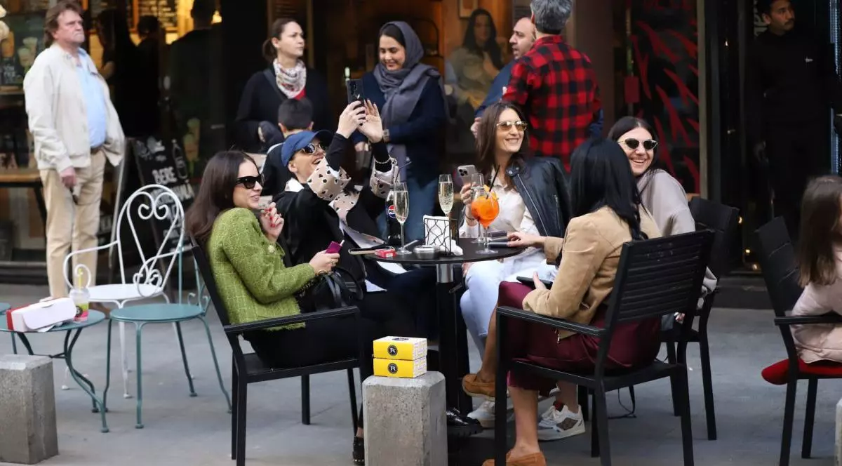 Un grup de cinci tinere stau la o masă, vorbesc, râd și fac poze, iar în jurul lor sunt alți oameni, în Centrul vechi, București, 13 aprilie 2025