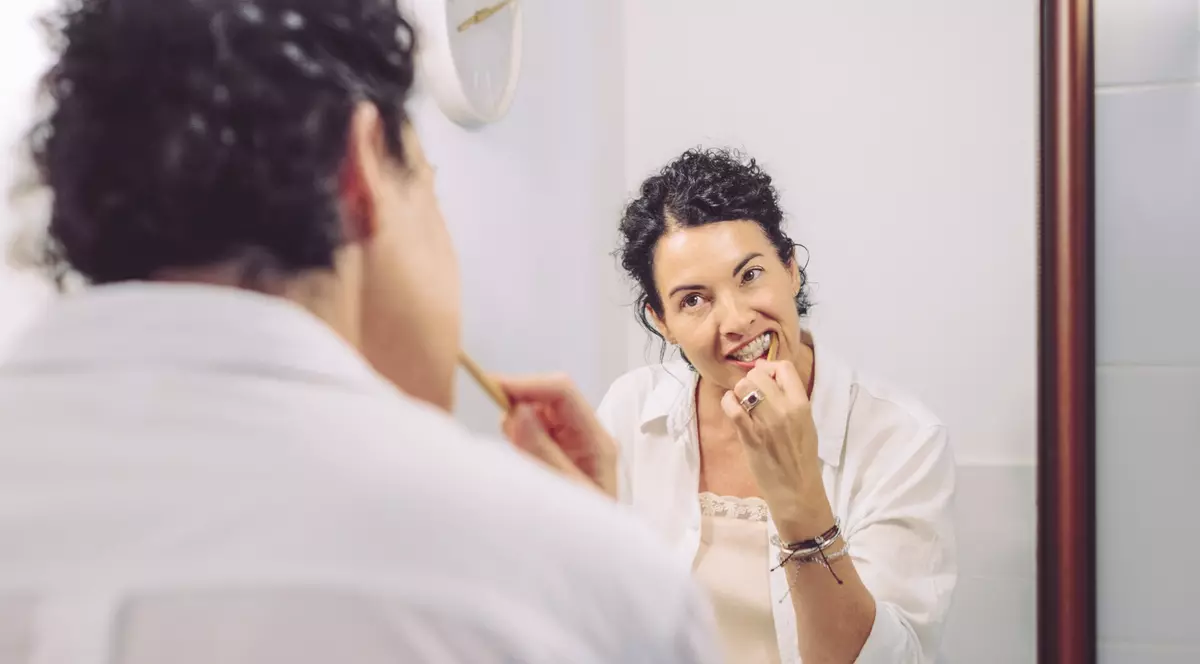 Regina Maria - femeie bruneta, imbracata cu o camasa alba, uitandu-se in oglinda in timp ce se spala pe dinti