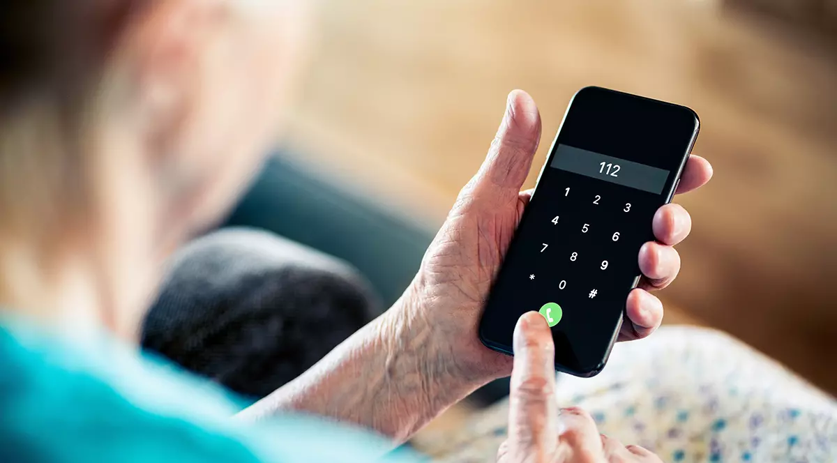 O femeie în vârstă care ține în mână un telefon și sună la 112