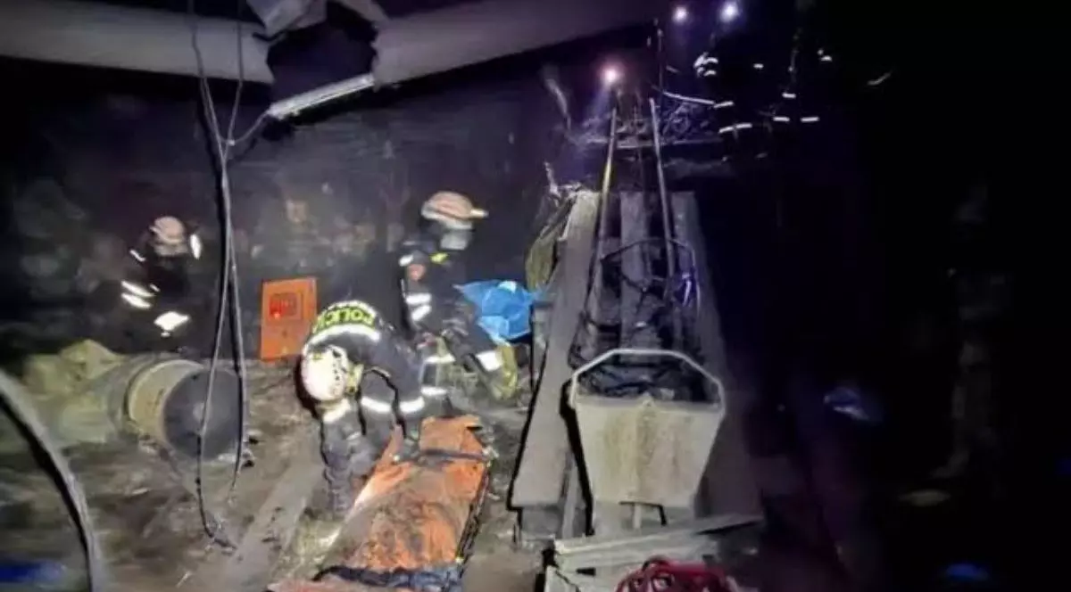 Imagini intunecate din interiorul unei mine cu doi asalvatori, unul in picioare si unul aplecat, mai multi scripeti in jur si lumina de la lanterne