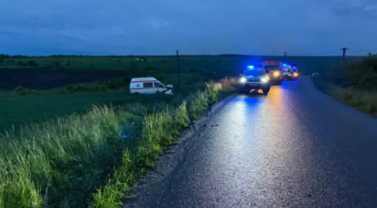 În partea stângă, într-un câmp, se observă o ambulanță ieșită complet de pe carosabil.
