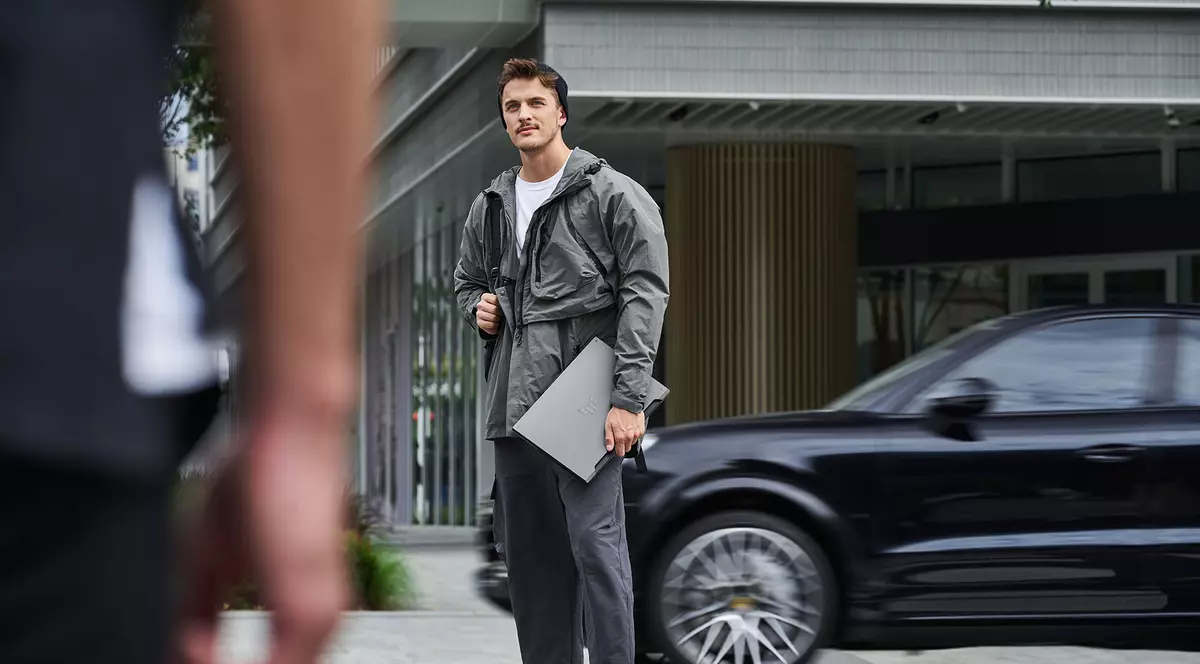 Baiat tanar, imbracat fashion, in fata unul bloc de birouri, tine in mana dreapta noul Asus TUF gamimg