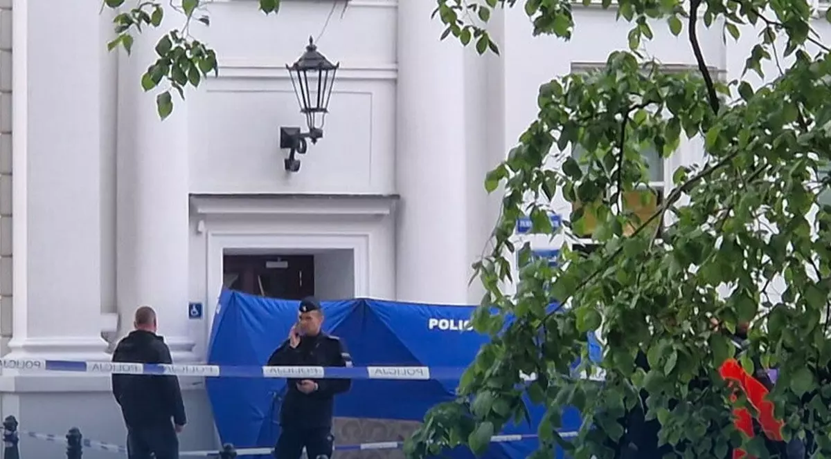 Doi polițiști la intrarea într-o clădire albă. O bandă galbenă izolează zona