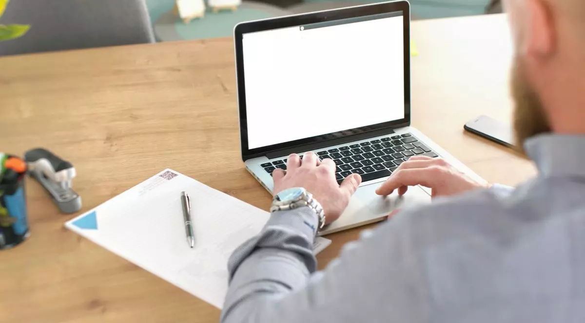 Bărbat anonim, neclar din spate, lucrând la laptop în birou, cu notebook, markere și calendar la birou, vedere din spate, detaliu pe mâini peste tastatură