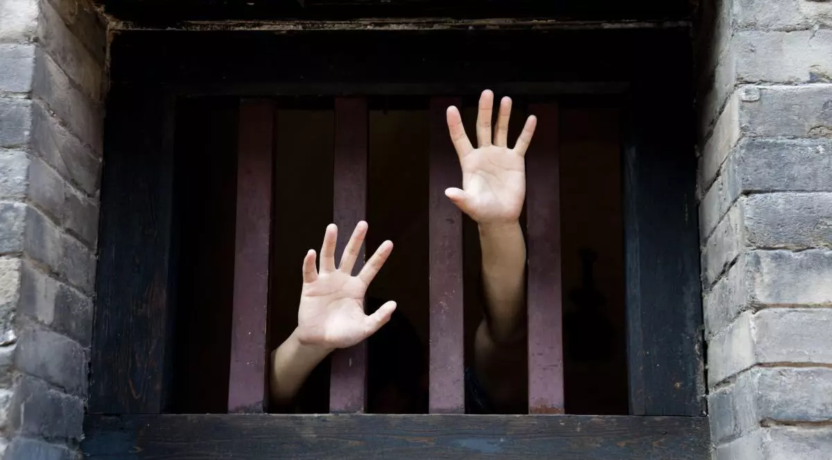 Mâinile unui bărbat aflat în închisoare ies printre gratiile de la fereastră, într-un strigăt de ajutor