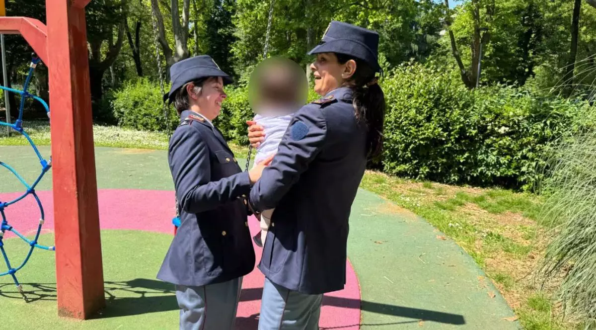 Două polițiste din Italia țin în brațe o bebelușă de 14 luni, a cărei față este blurată, după ce micuța a fost găsită în condiții teribile
