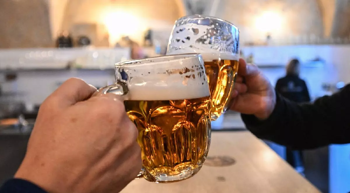 Doi bărbați își ciocnesc halbele pline cu bere „Pilsner Urquell” în pub-ul „U Rarasku” din Praga, Republica Cehă, pe 19 martie 2025