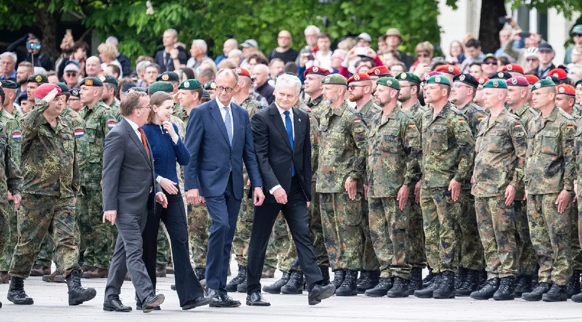 Patru bărbați îmbrăcați în costume negre, în fața unei mulțimi de soldați