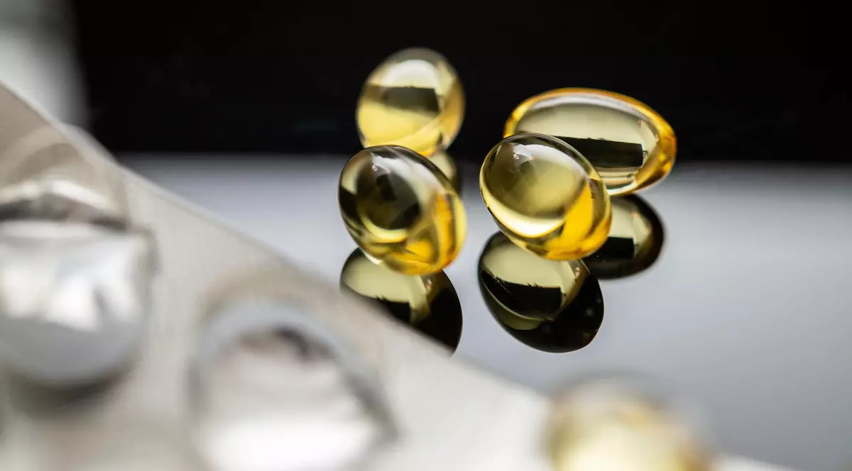 Poză cu patru capsule galbene transparente care conțin vitamina D și ulei de pește