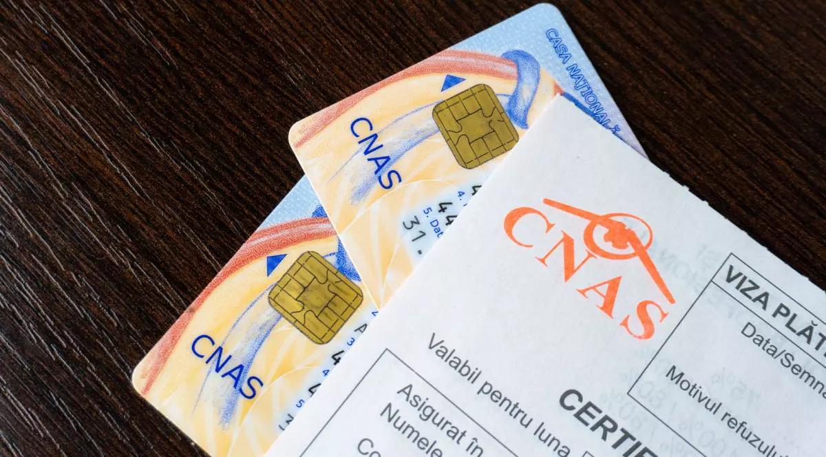 Imagine creativă cu două carduri de sănătate acoperite de o rețetă cu logo-ul CNAS, pe un birou negru