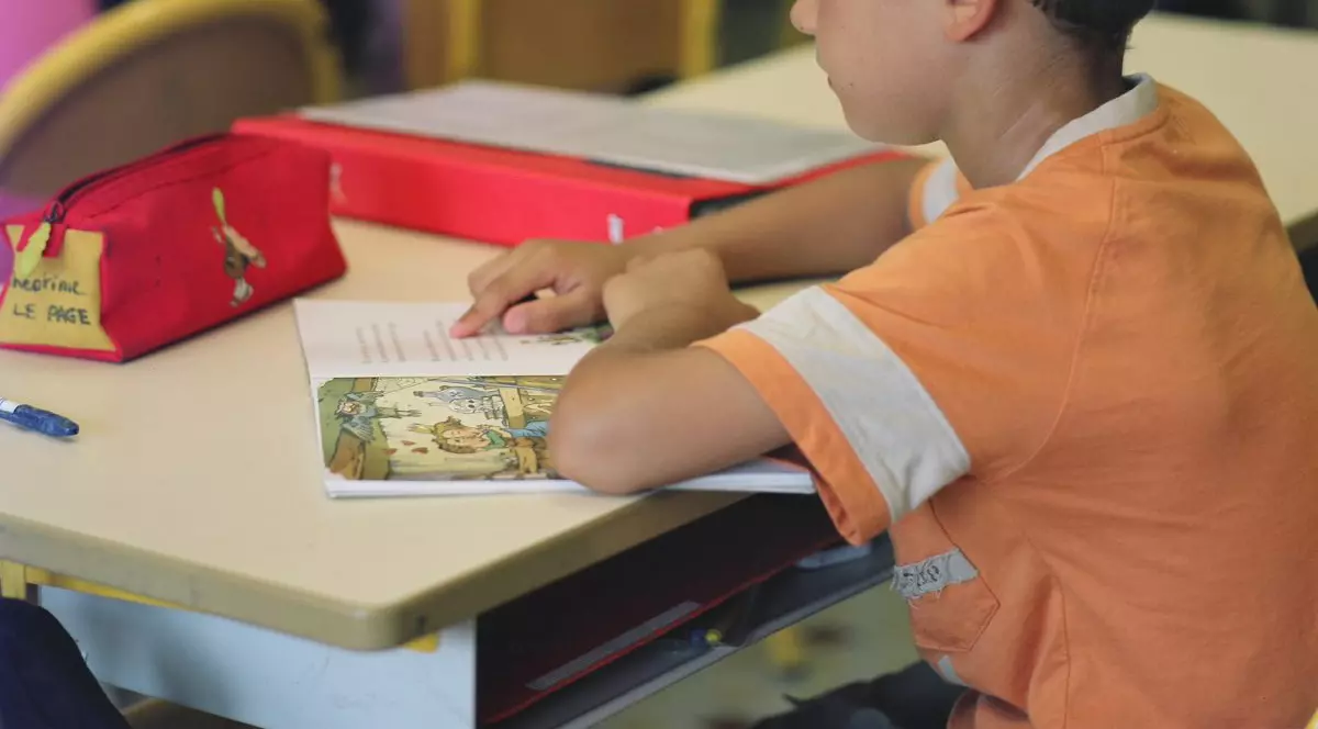 Elev de vârstă mică îmbrăcat într-un tricou portocaliu stă în bancă și citește