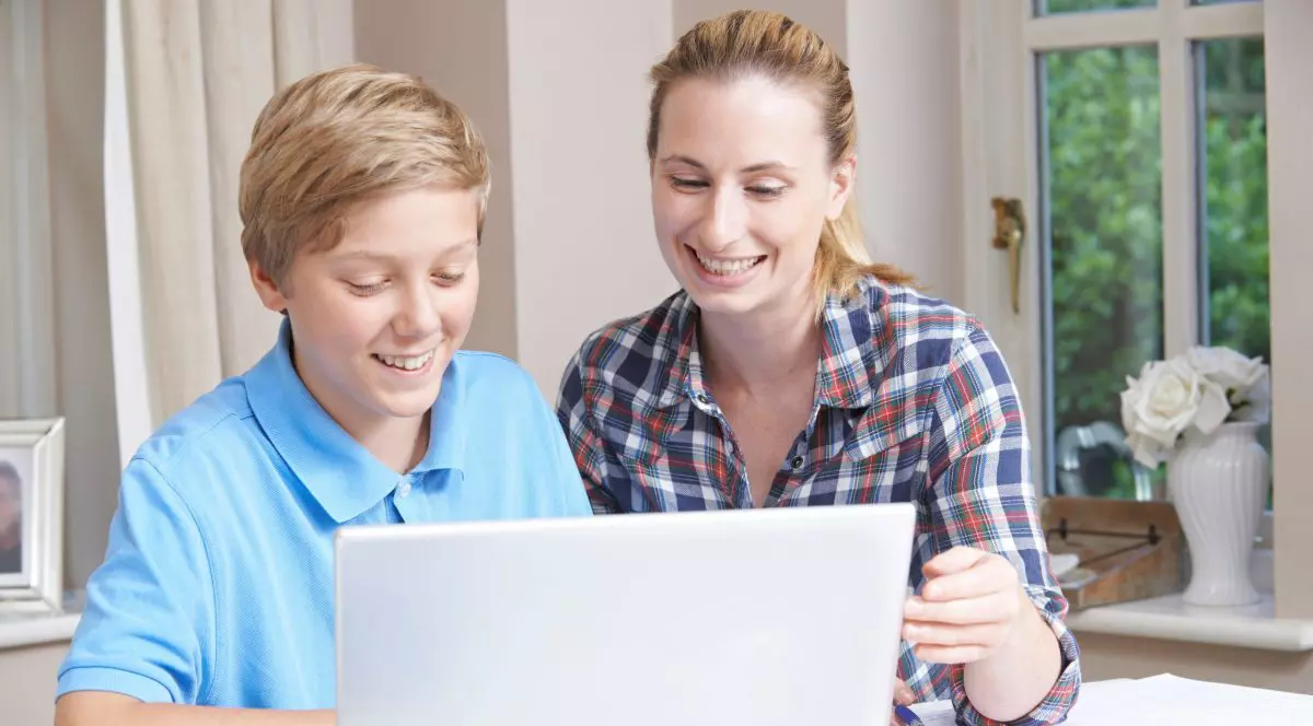 Un baiat sta alaturi de mama sa în fata unui laptop si zambesc