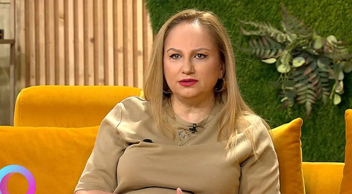 Astrologul Cristina Demetrescu, îmbrăcată cu o bluză maro, stă pe o canapea portocalie în studioul unei emisiuni TV