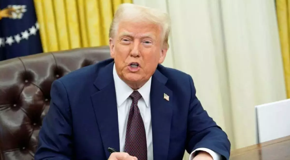 În imagine este ilustrat Donald Trump, îmbrăcat în sacou albastru închis, cămașă albă și cravată maro. Acesta se află la birou, în timp ce ține un pix în mână