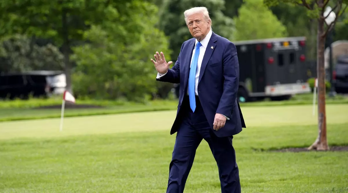 Donald Trump îmbrăcat în costum bleumarin, cămașă albă și cravată bleu, face cu mâna. Președintele american Donald Trump se plimbă pe peluza de sud a Casei Albe din Washington înainte de plecarea sa în Alabama pe 1 mai 2025.